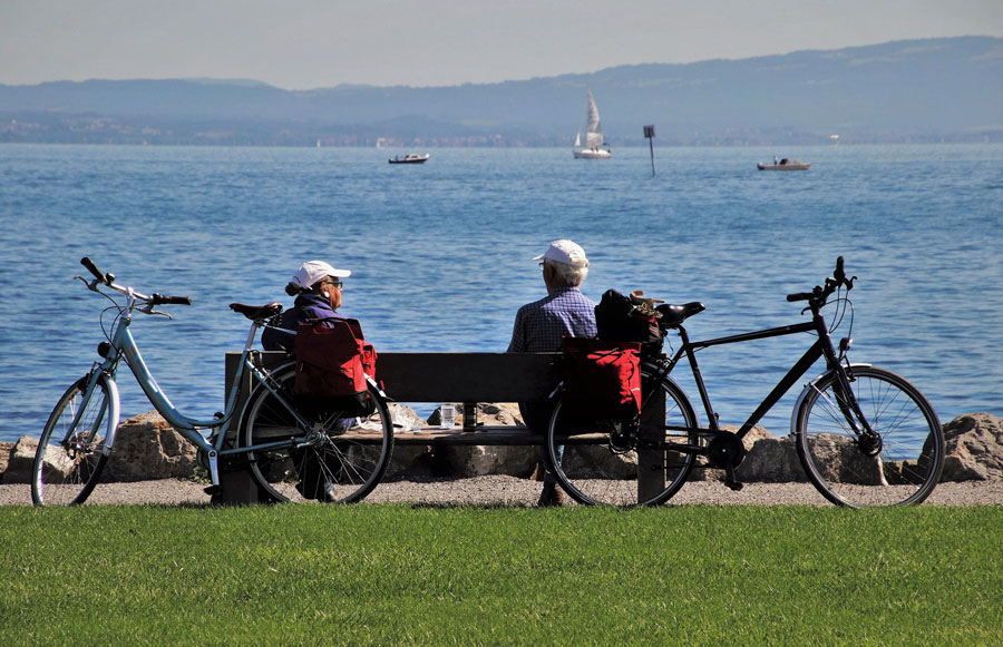 Fahrradtour - Ein Paar auf einer Bank am Bodensee. Im Hintergrund sind Schiffe zu sehen.